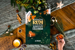 
                  
                    The Australian rum advent calendar box staged on a wooden table with some local plants, a rum glass, candles and festive decorations
                  
                